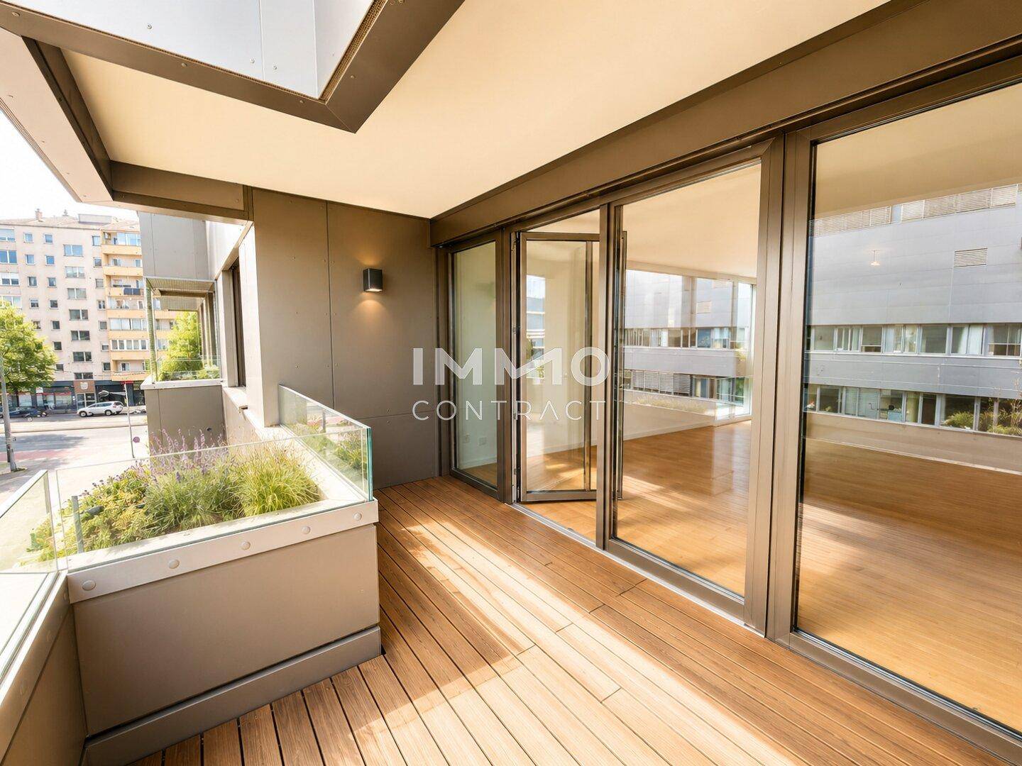 Moderner Balkon mit Holzdeck, Glasgeländer und Blick auf die Stadtstraße.