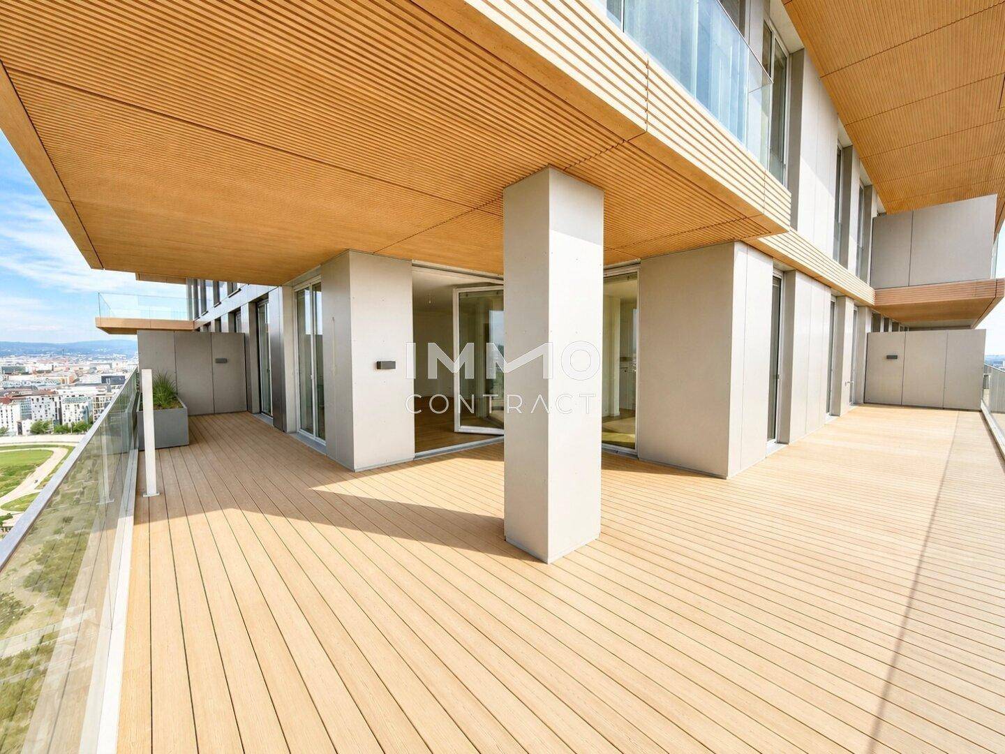 Geräumige Terrasse mit Holzdeck und moderner Architektur, umgeben von Glasgeländern und viel Grün.