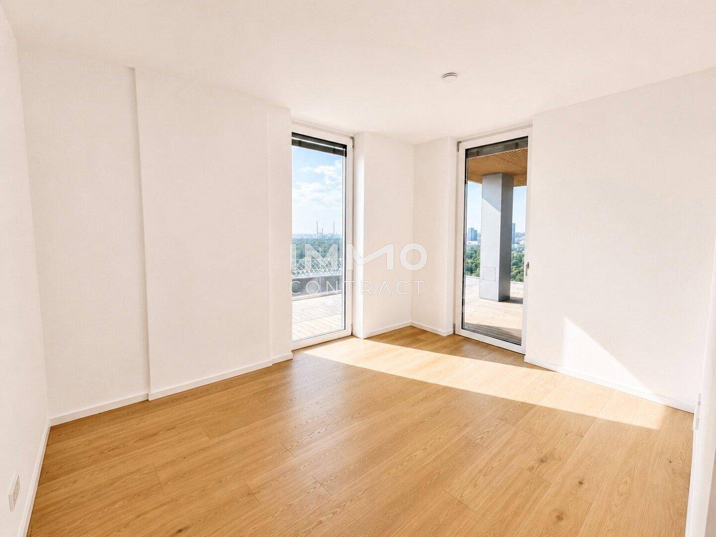 Helles Schlafzimmer mit Parkettboden und Zugang zu einem Balkon, bietet einen weiten Ausblick.