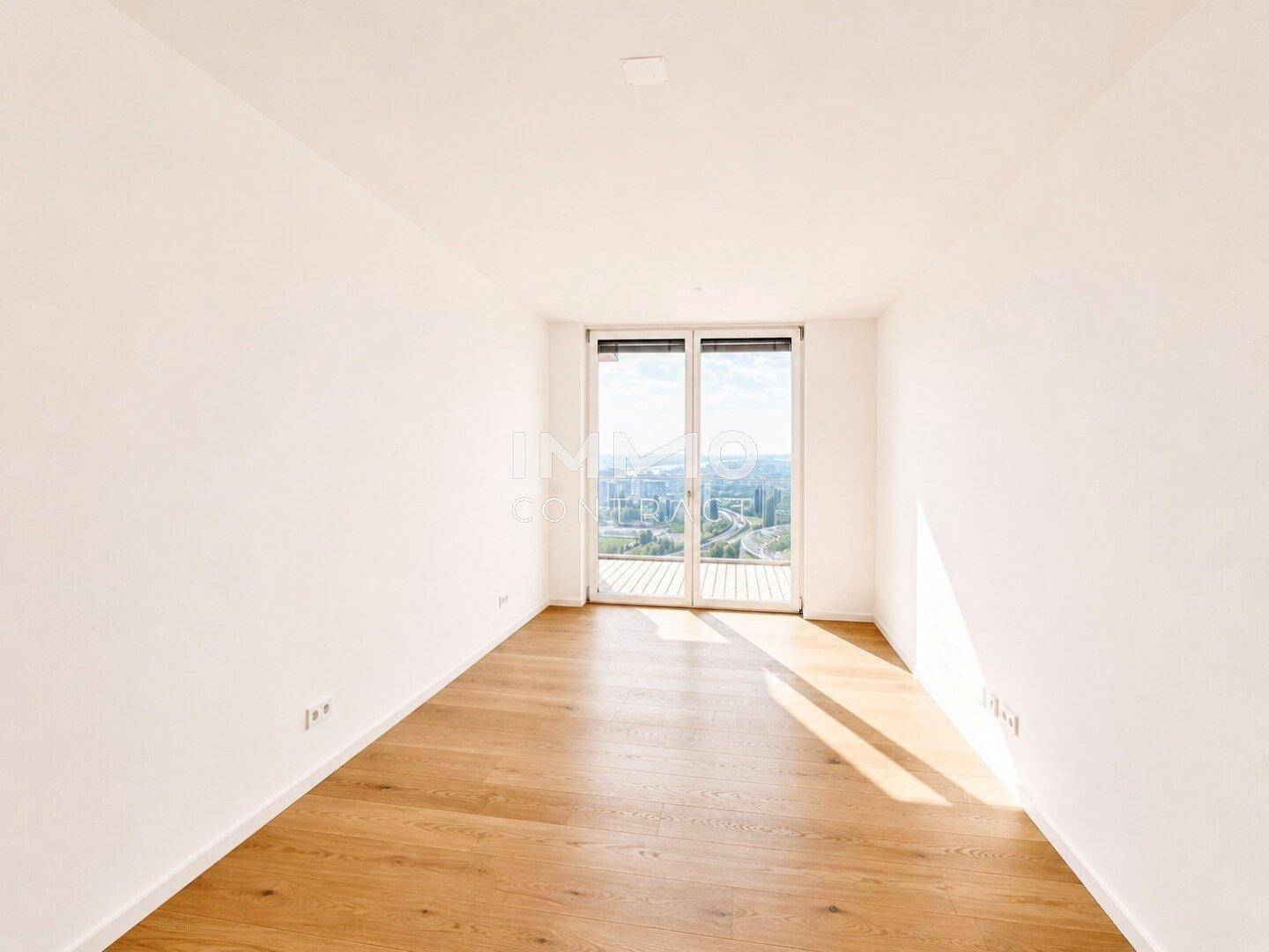 Helles Schlafzimmer mit Parkettboden und Zugang zu einem Balkon, bietet einen weiten Ausblick.