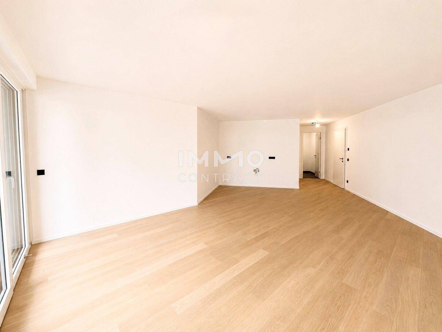 Geräumiger Wohnbereich mit hellem Holzboden und großen Fenstern, die den Raum mit Licht füllen.