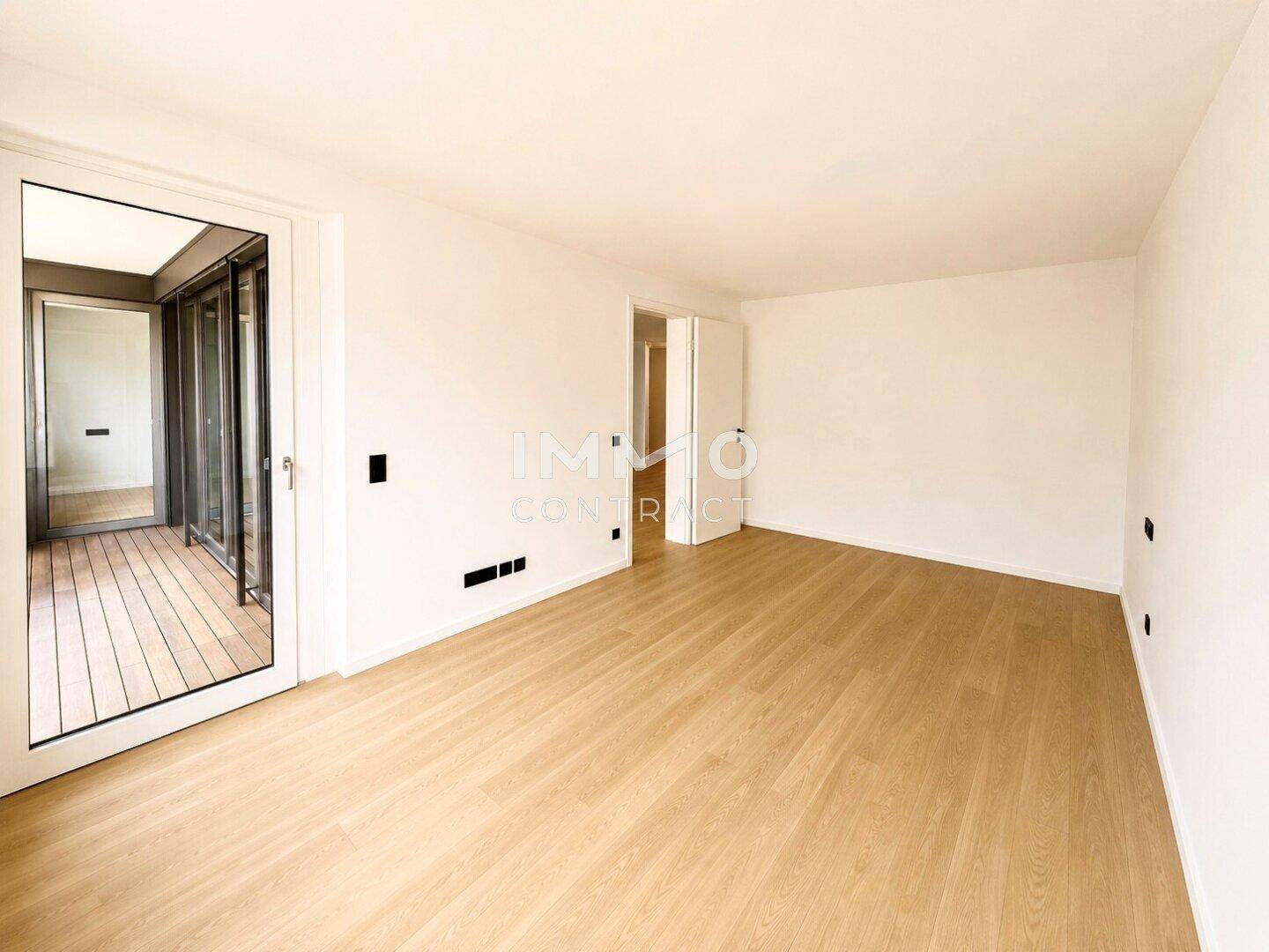 Helles Zimmer mit Holzboden und einer großen Glastür, die den Blick auf den Außenbereich freigibt.