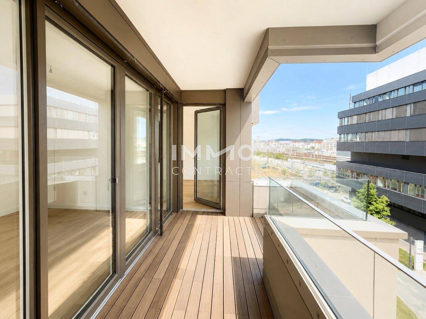 Moderner Balkon mit Holzbelag und Glasgeländer bietet einen weiten Blick über die Stadt.