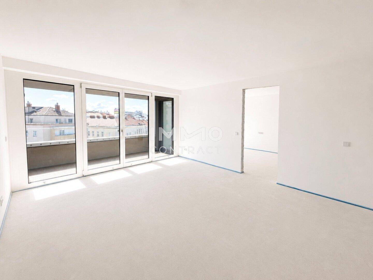 Geräumiger, unmöblierter Wohnbereich mit großen Fenstern und Zugang zu einem Balkon.