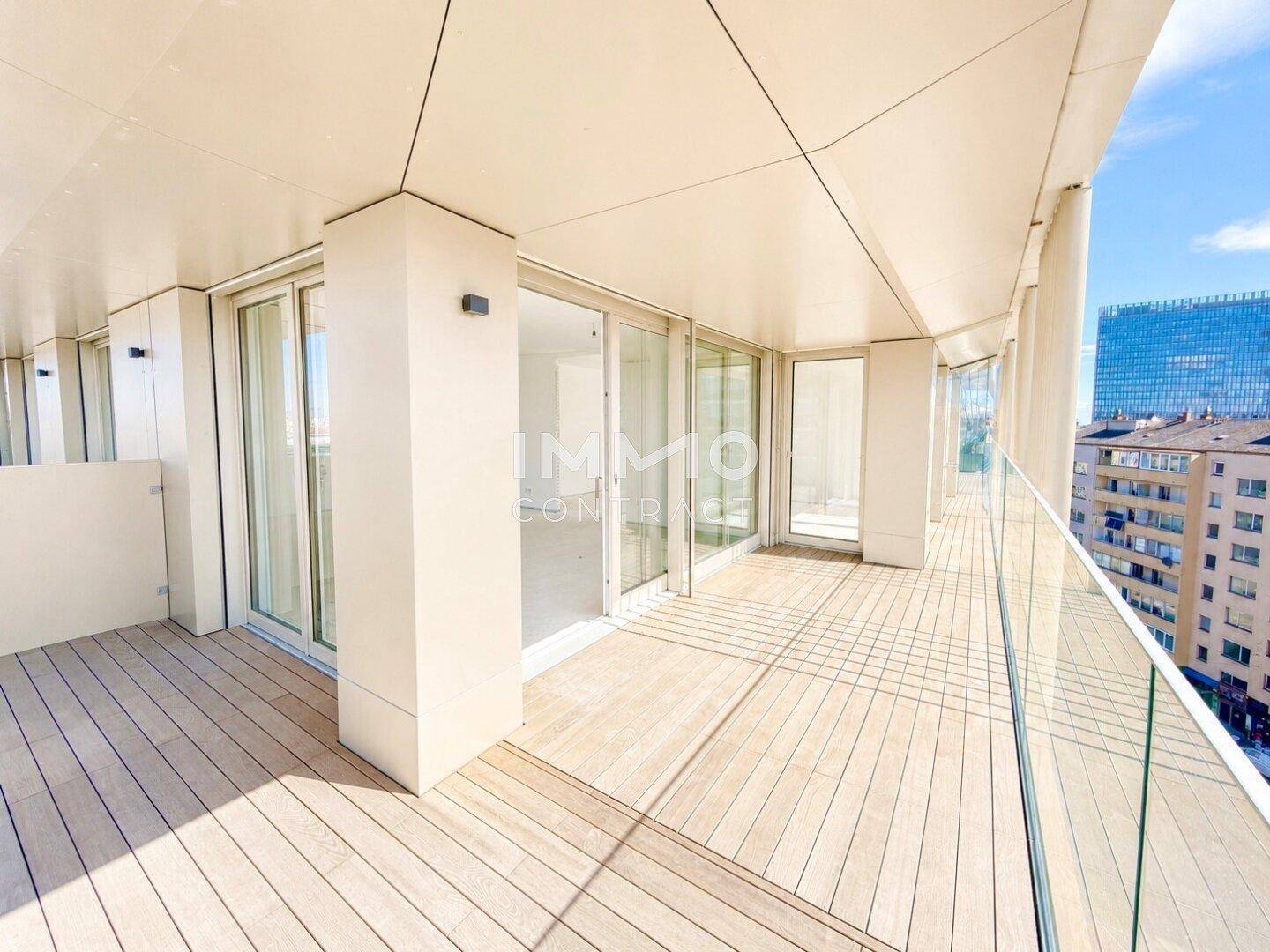 Geräumiger Balkon mit Holzboden und Glasgeländer, bietet einen weiten Blick über die Stadt.
