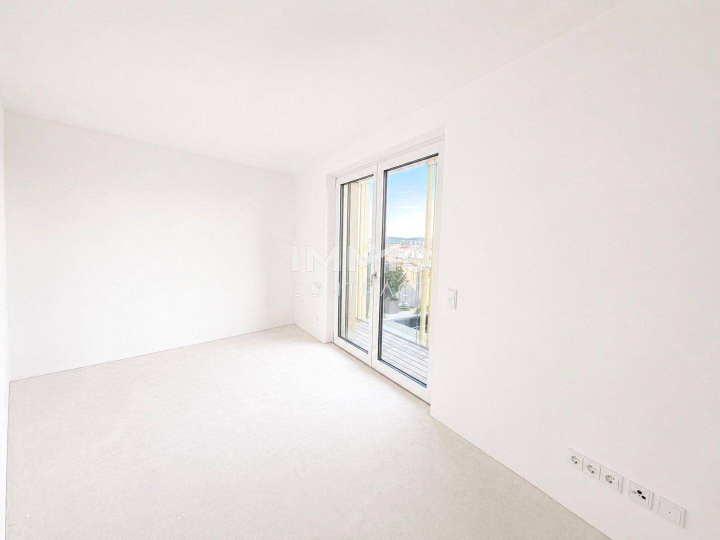 Helles, unmöbliertes Zimmer mit großem Fenster und Zugang zu einem Außenbereich.