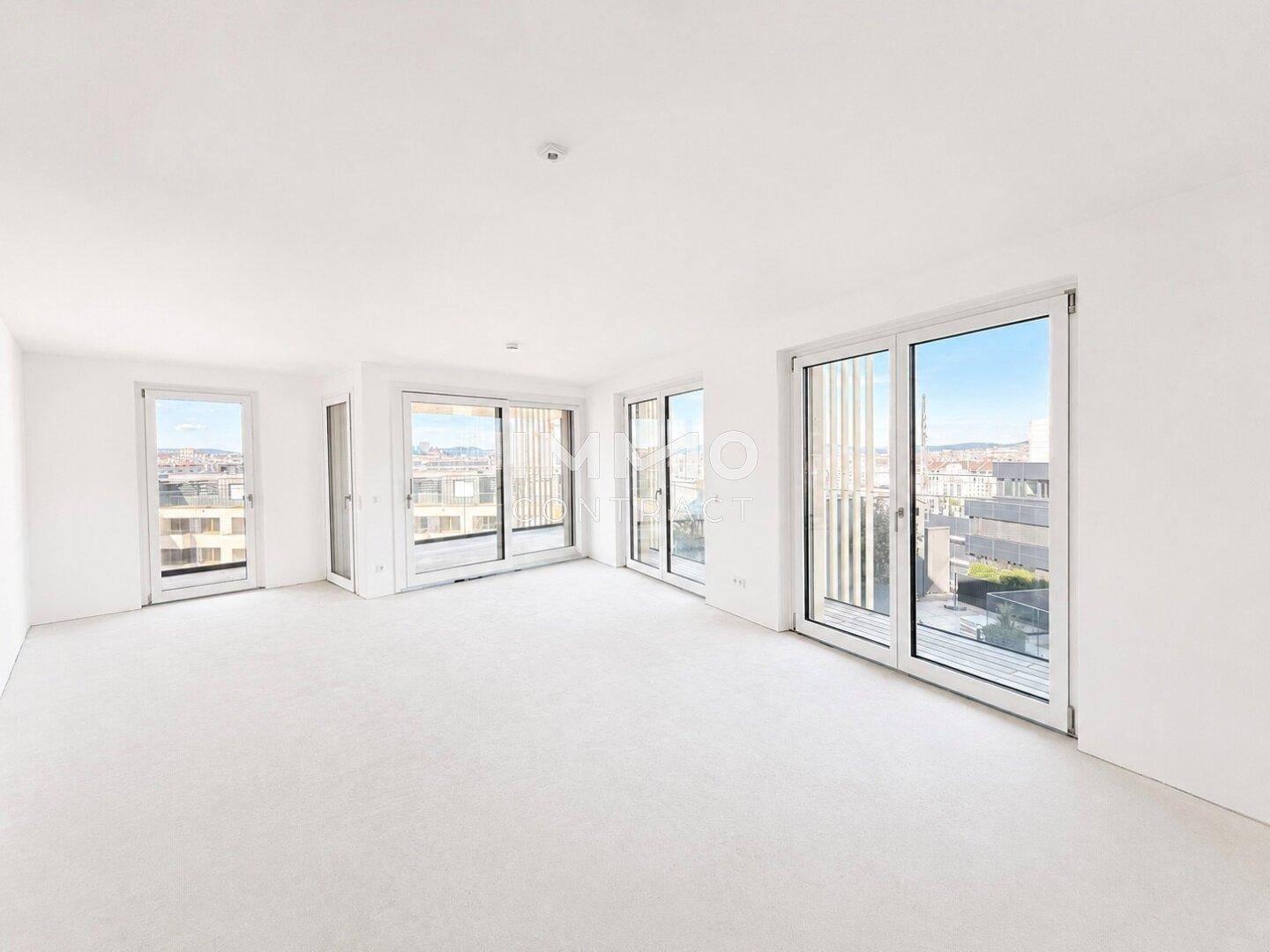 Heller, unmöblierter Wohnraum mit großen Fenstern, hohen Decken und urbanem Ausblick.