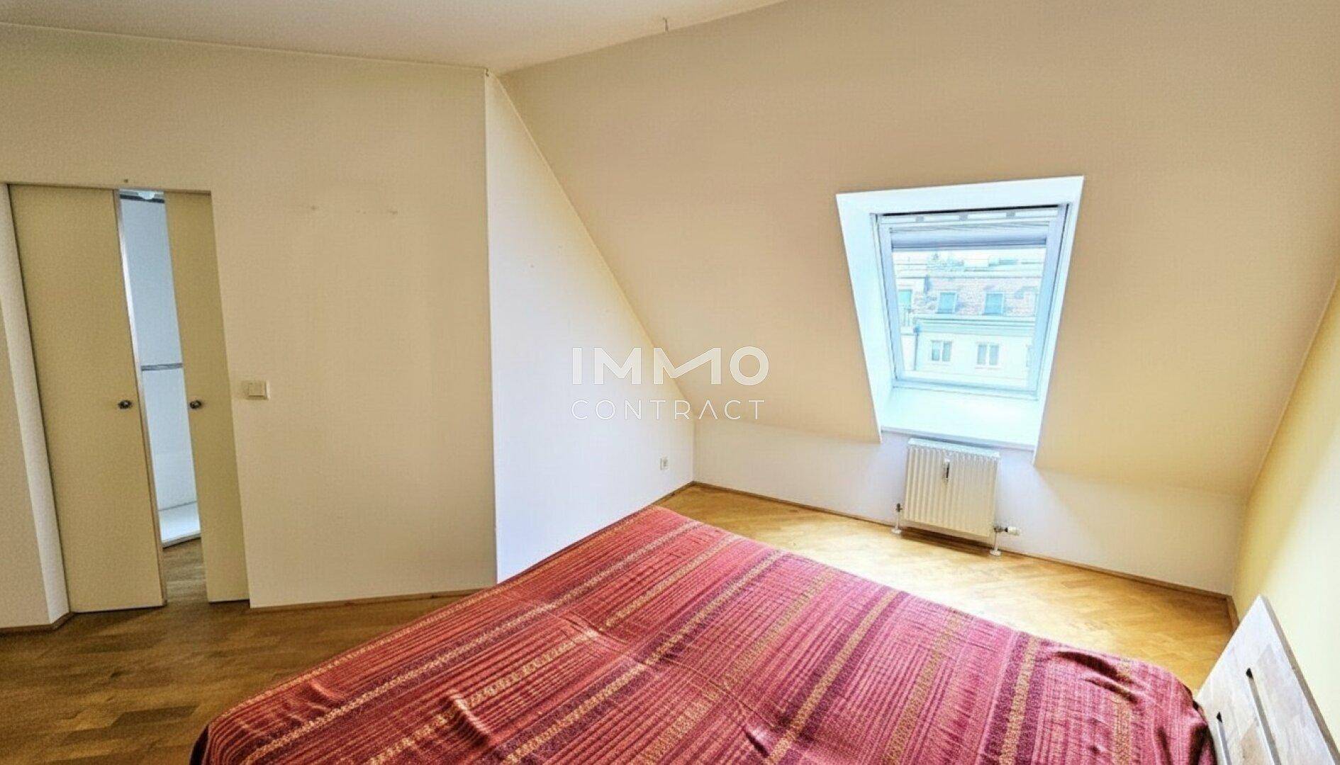 Schlafzimmer mit Holzboden, Dachfenster und Zugang zu einem weiteren Raum.