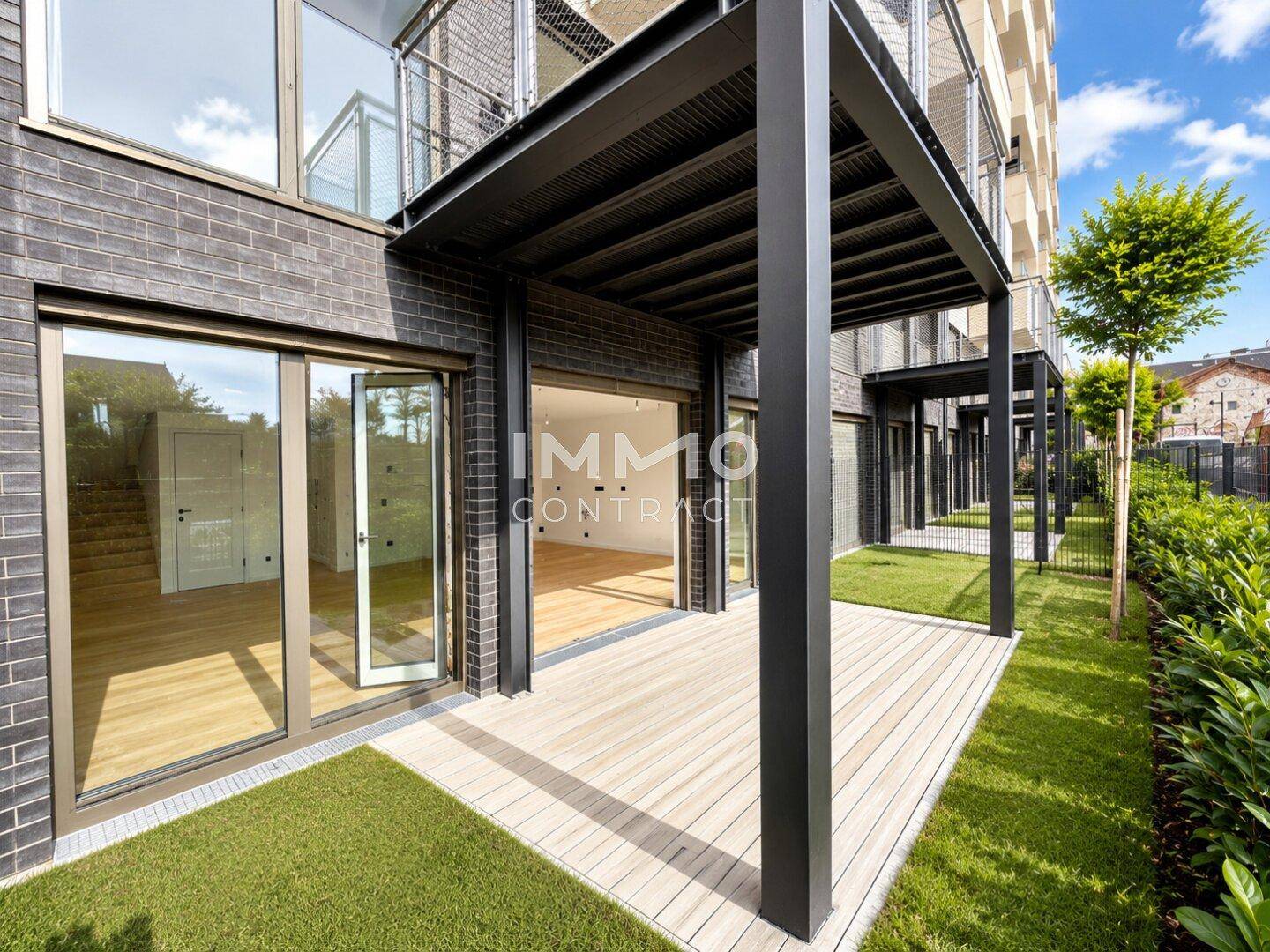 Erdgeschoss-Terrasse mit Holzdeck und Rasenfläche vor einer modernen Ziegelfassade.