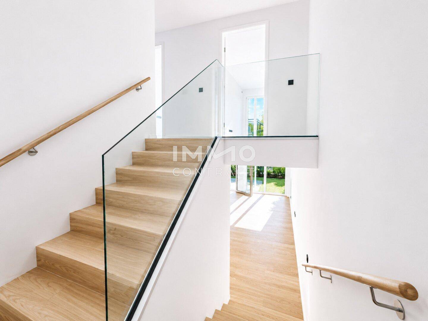 Moderne Holztreppe mit Glasgeländer in einem lichtdurchfluteten Eingangsbereich.