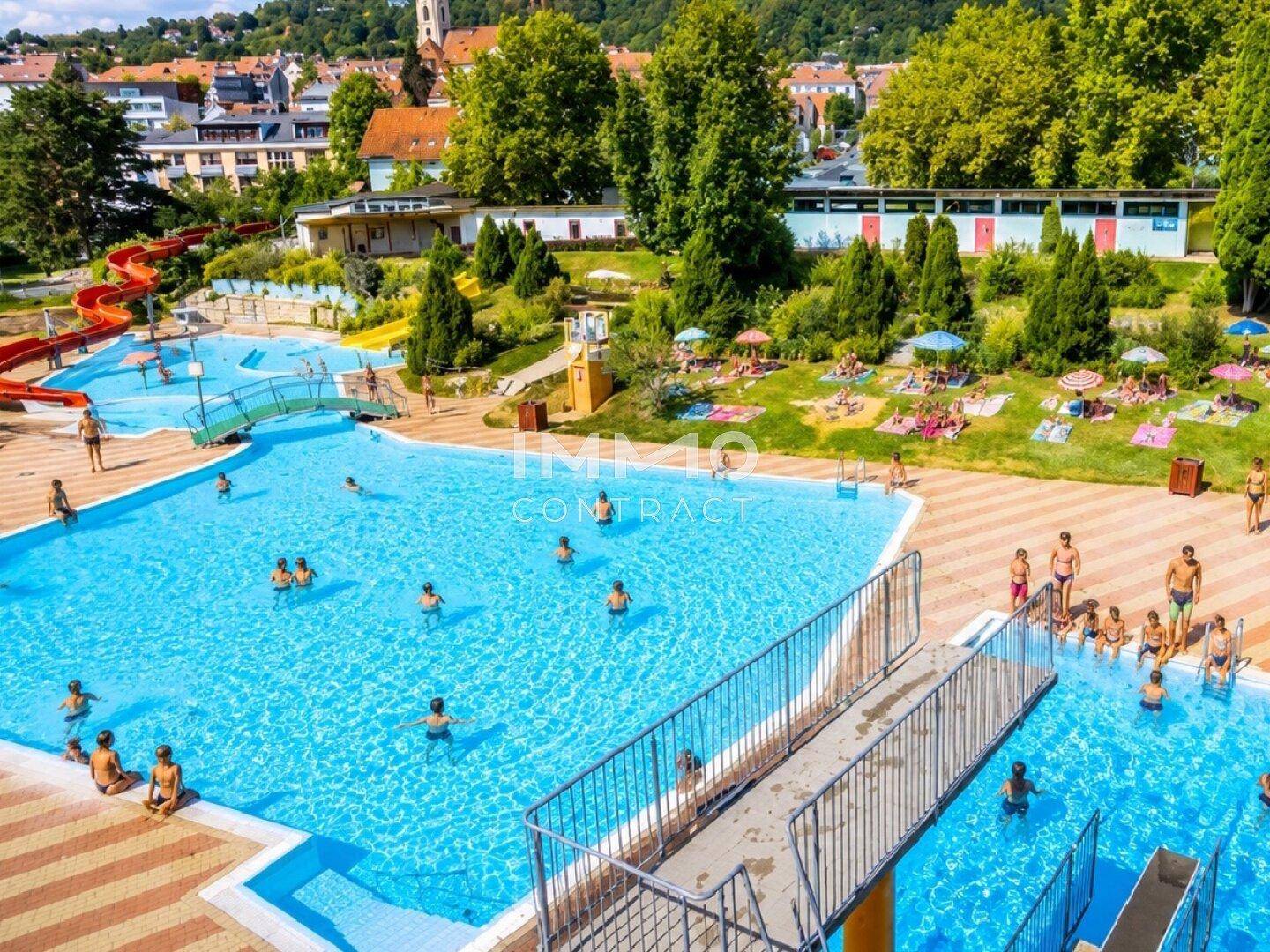 Großes Freibad mit mehreren Becken, Wasserrutschen und Liegewiesen für Besucher.