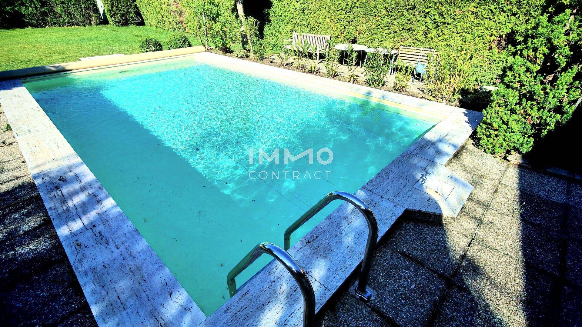 Großer Swimmingpool mit sauberem Wasser, umgeben von gepflegten Steinplatten und Hecken.
