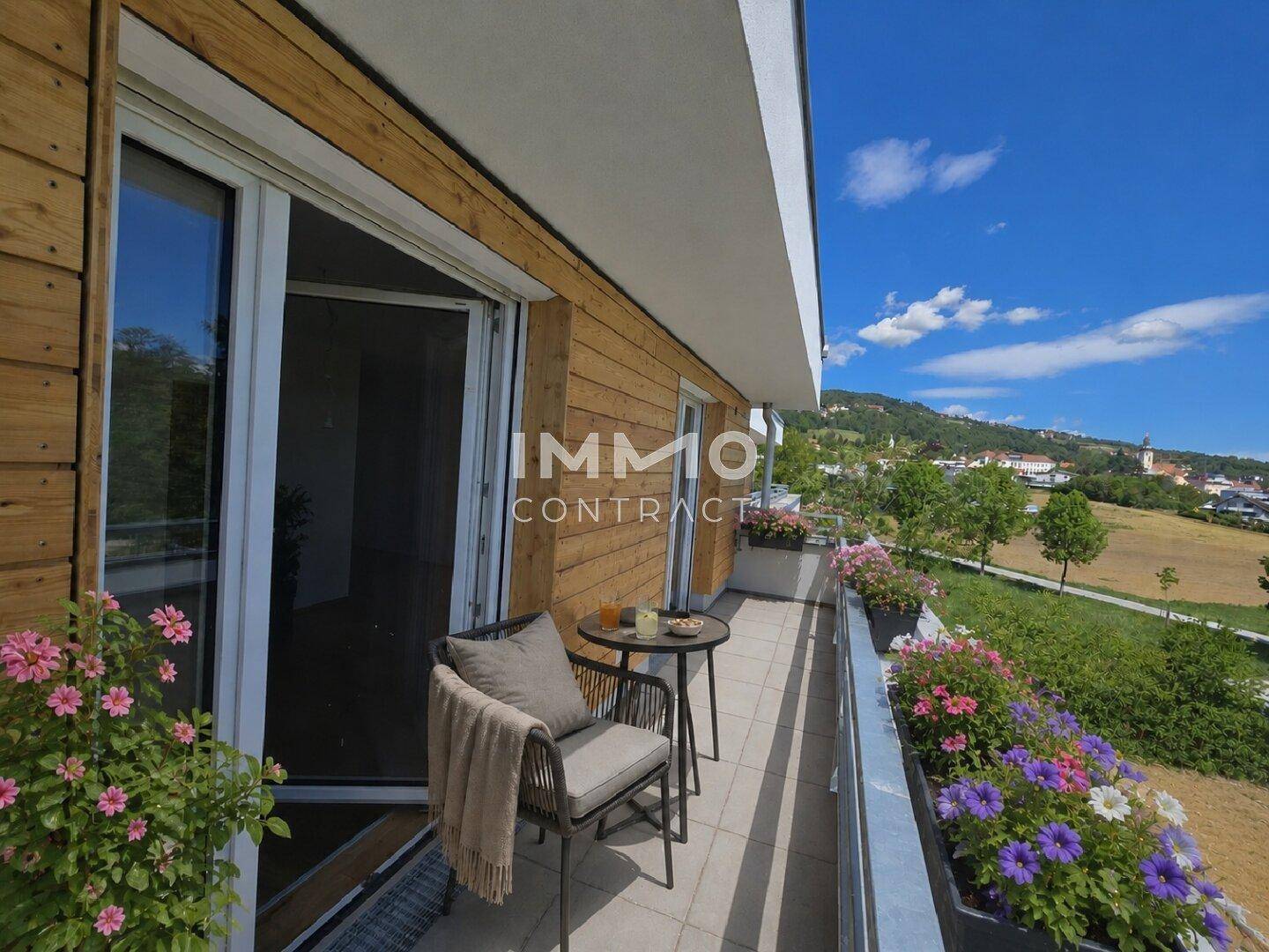 Gemütlicher Balkon mit Sitzgelegenheit und weitem Blick über die Landschaft und ein Dorf.