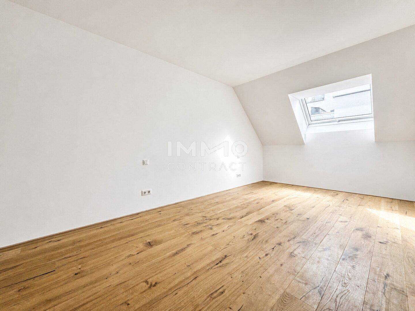 Geräumiges Zimmer im Dachgeschoss mit Holzboden und einem Dachfenster für natürliches Licht.
