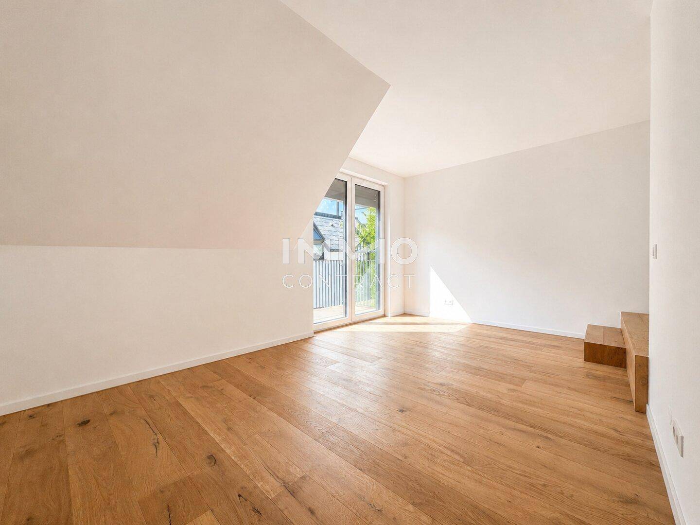 Helles Zimmer im Dachgeschoss mit Holzboden und Zugang zu einem kleinen Balkon.