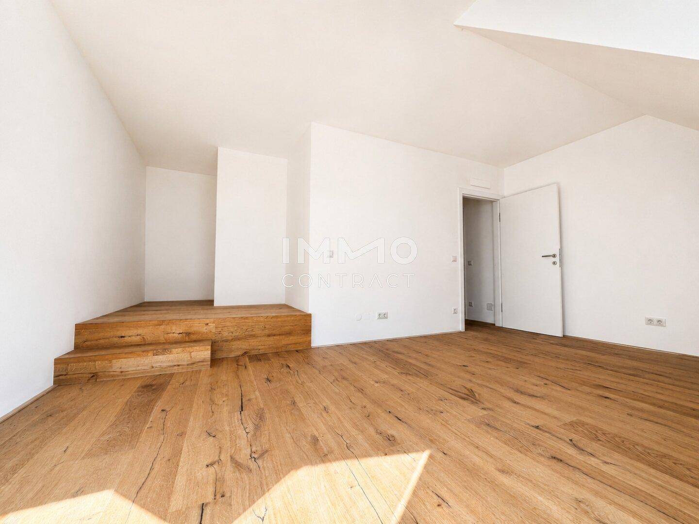 Geräumiges Zimmer im Dachgeschoss mit Holzboden und einer erhöhten Holzplattform.