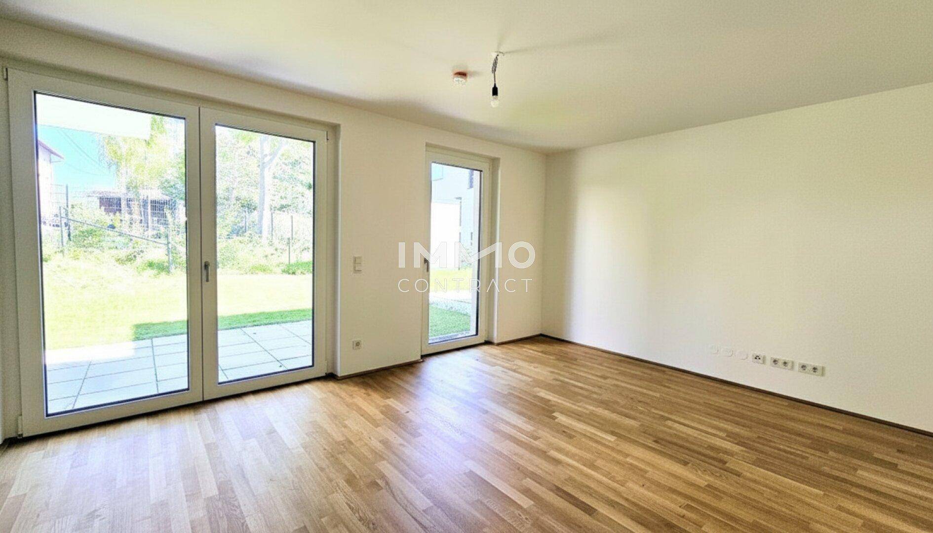 Helles Wohnzimmer mit Holzboden und großen Glastüren, die auf die Terrasse und den Garten führen.
