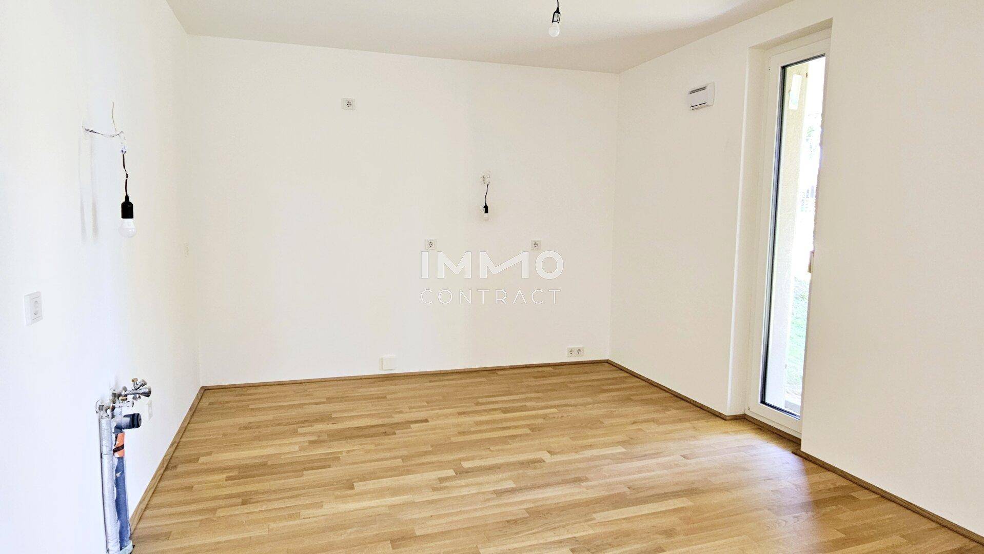 Leerer Raum mit Holzboden und Anschlüssen für eine zukünftige Küche oder einen Hauswirtschaftsraum.