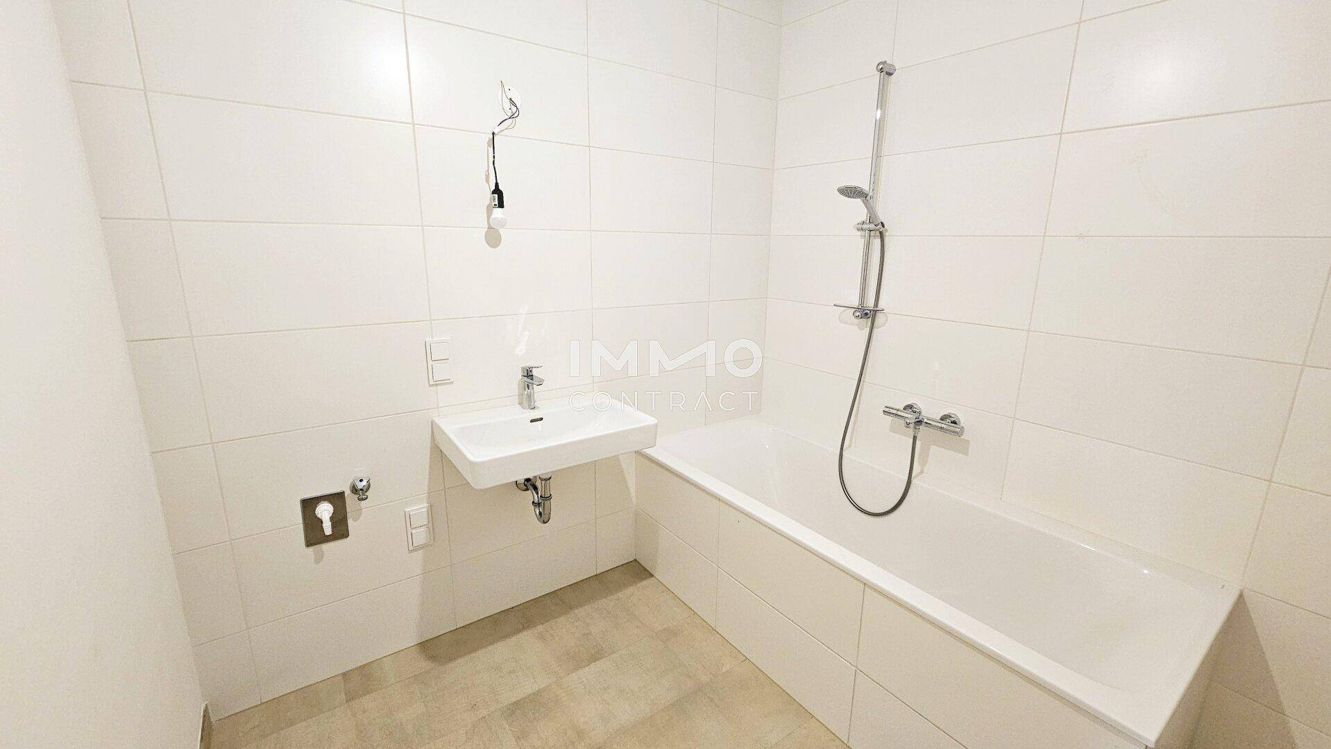 Modernes Badezimmer mit weißen Fliesen, Badewanne und Waschbecken, in neuwertigem Zustand.