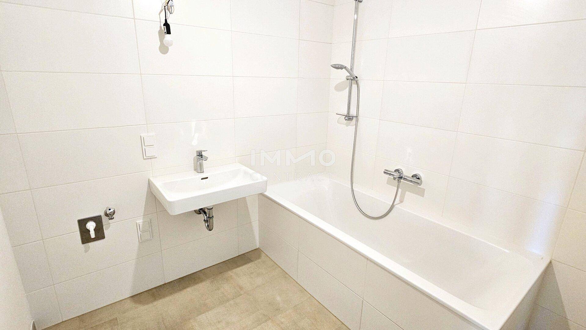 Modernes Badezimmer mit weißen Wandfliesen, Badewanne mit Duschfunktion und Waschbecken.