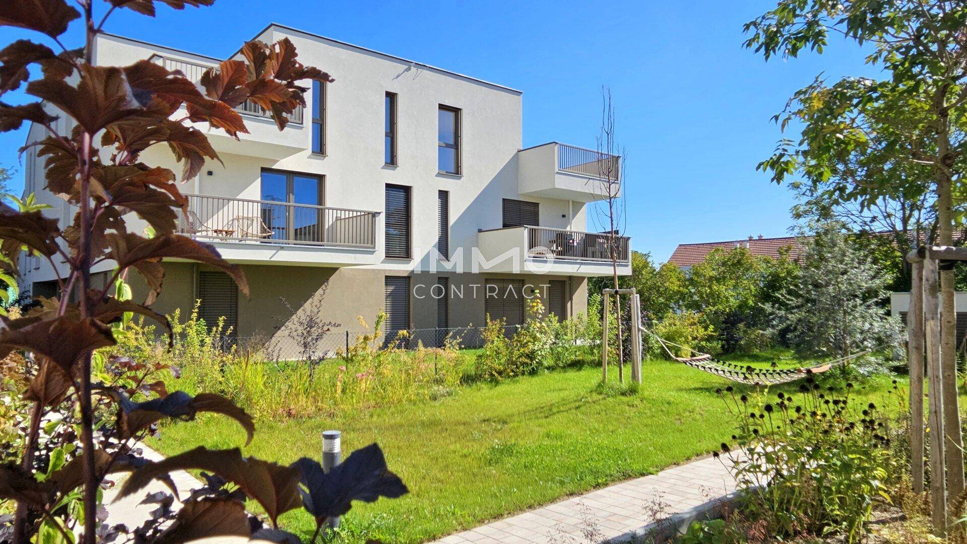 Moderne Wohngebäude mit Balkonen und einer ansprechenden, sonnigen Gartenlandschaft.