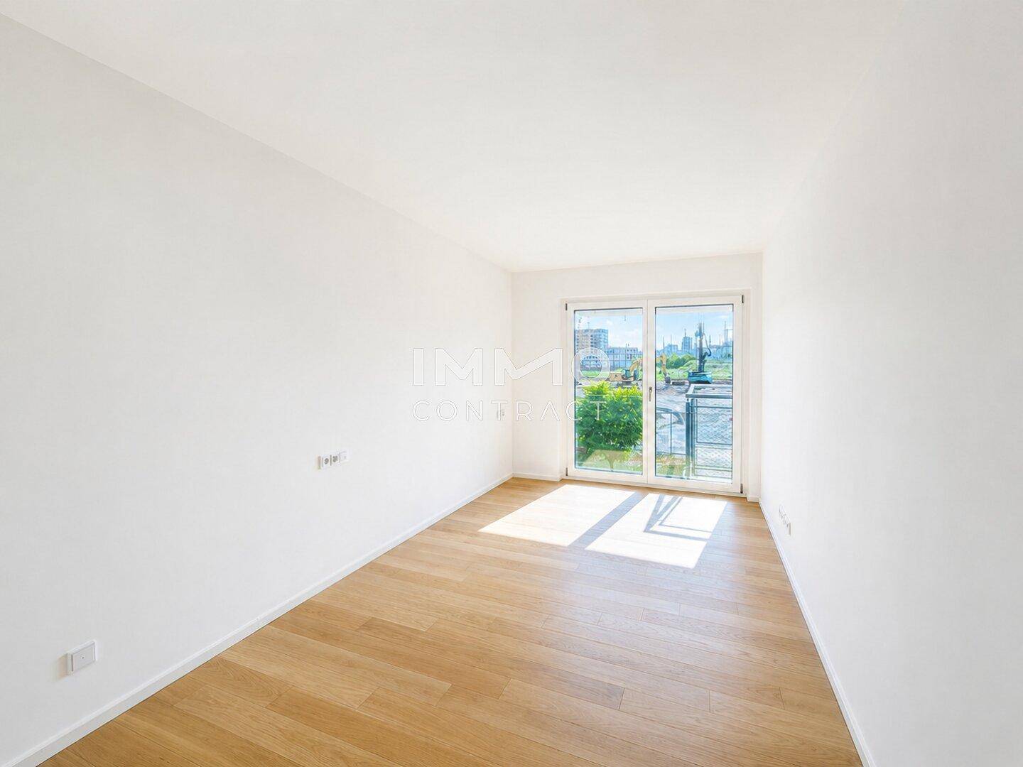 Helles, unmöbliertes Zimmer mit Holzboden und Fenster, das viel Sonnenlicht hereinlässt.