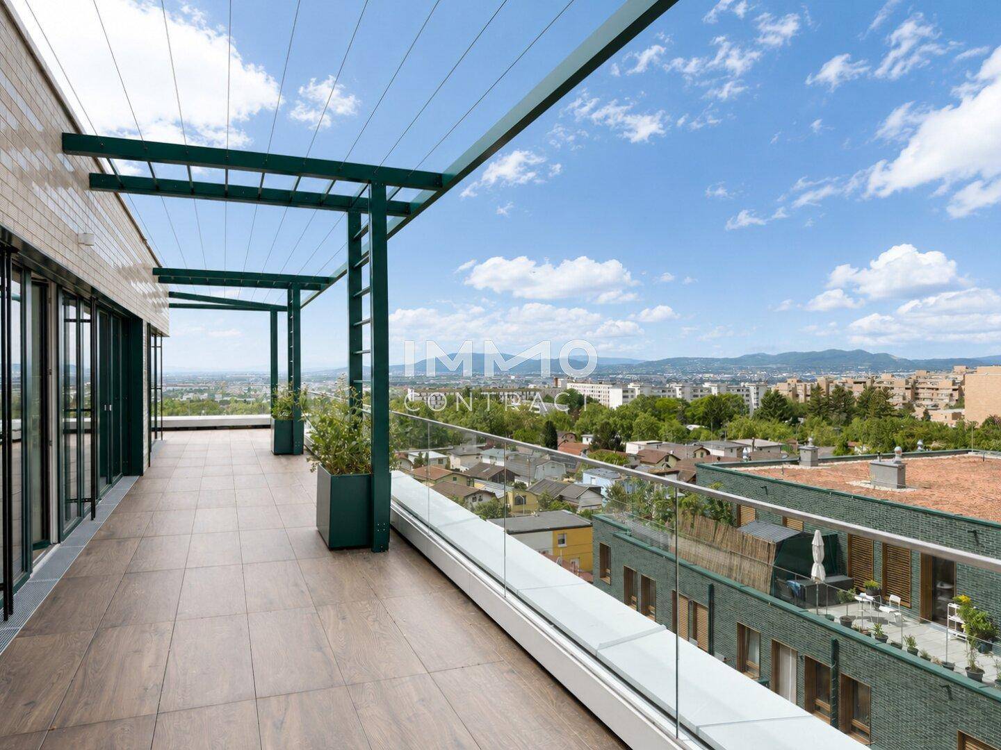 Weitläufige Dachterrasse mit Fliesenboden, Glasbrüstung und Pergola mit Panoramablick über die Stadt.