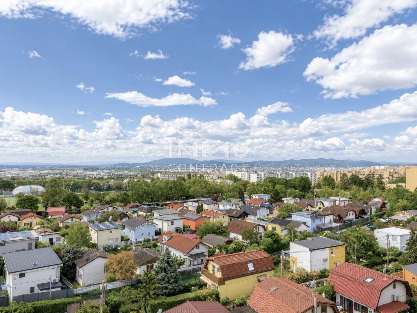 Weitläufiger Blick über eine Wohnsiedlung mit vielen Häusern und grünen Flächen unter blauem Himmel.
