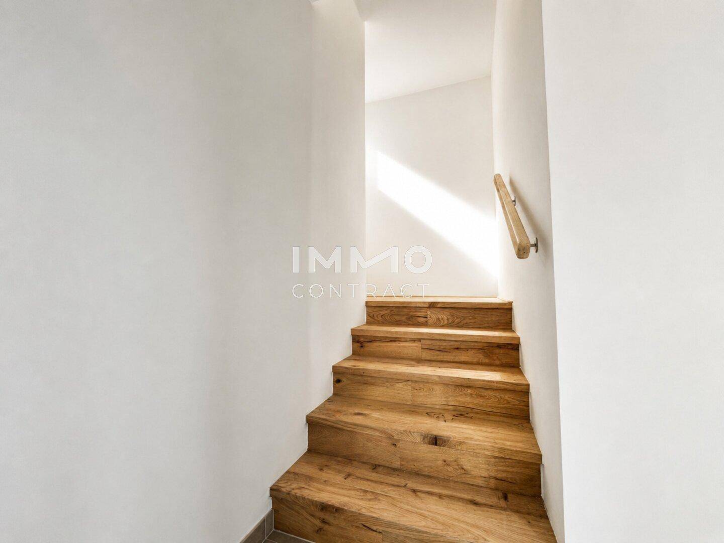 Elegante Holztreppe mit schlichtem Holzgeländer, die die verschiedenen Ebenen des Hauses verbindet.
