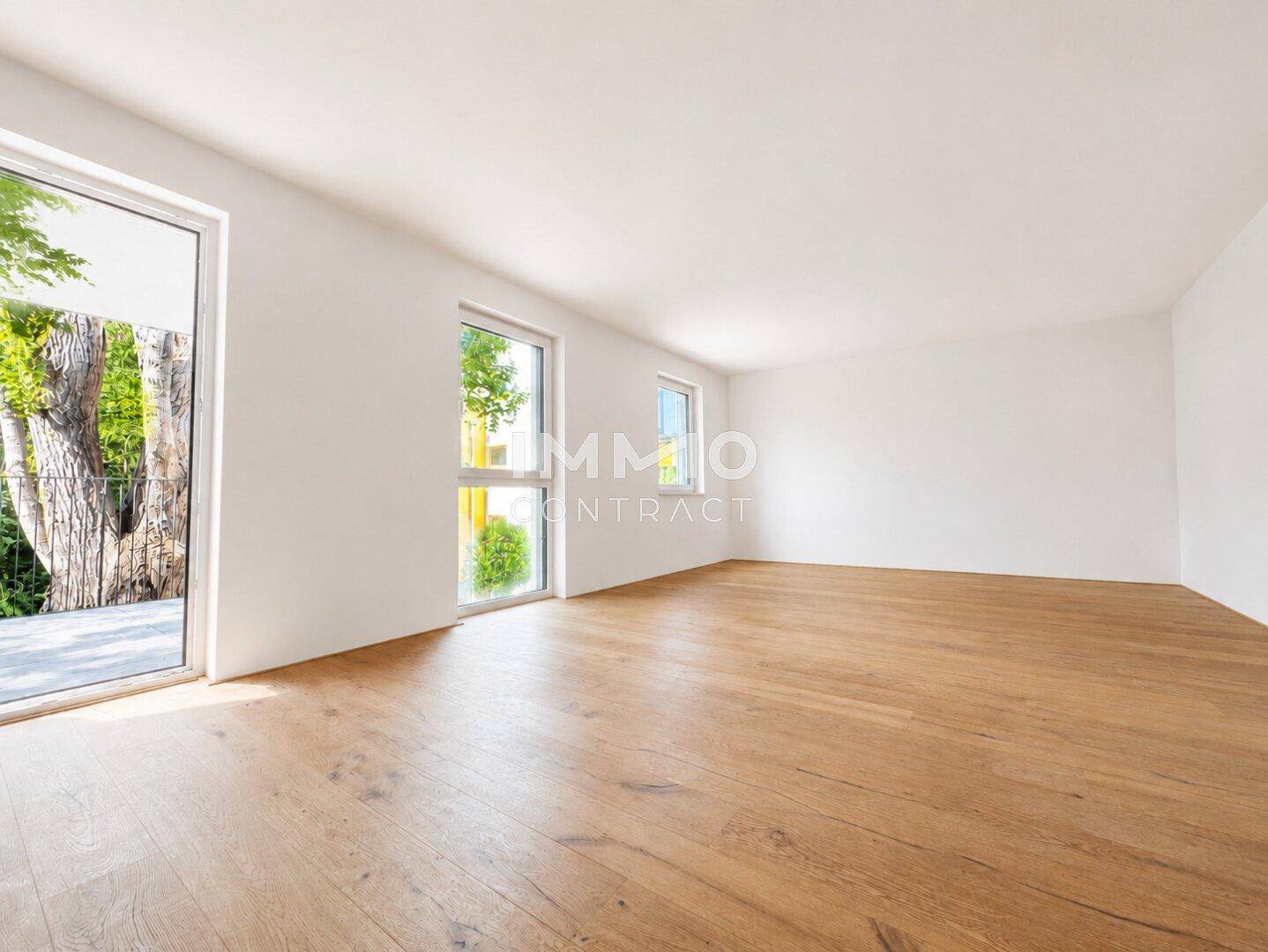 Geräumiges, unmöbliertes Zimmer mit Holzboden und großen Fenstern, die viel Tageslicht hereinlassen.