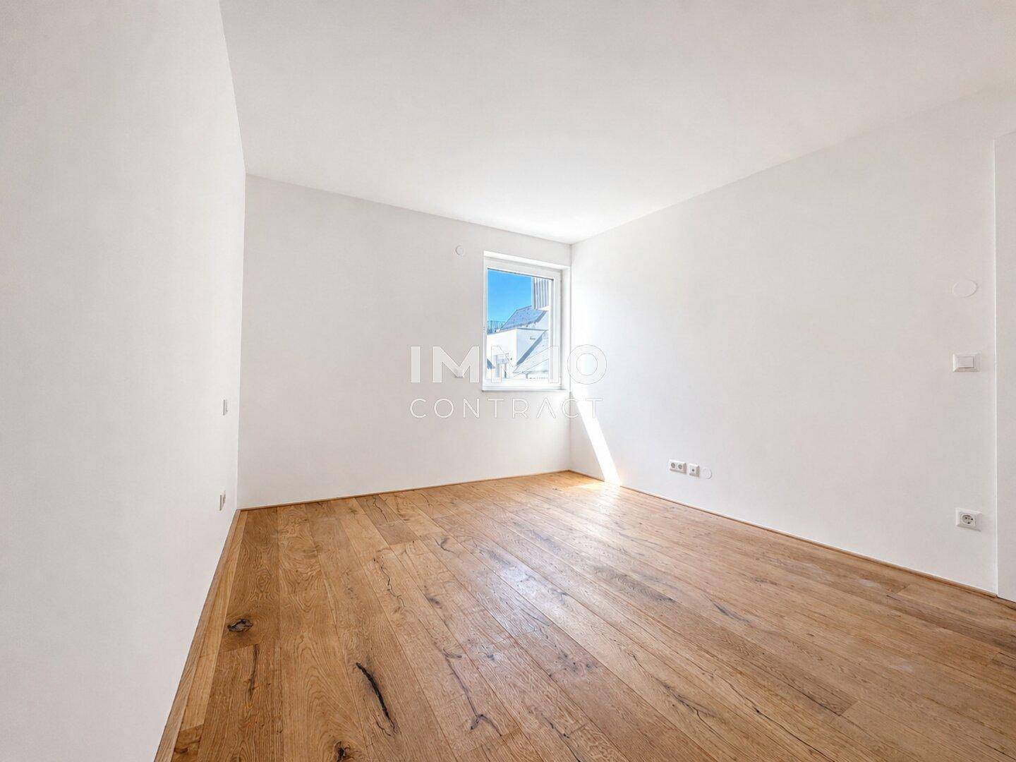 Leeres Zimmer mit Holzboden und einem Fenster, das einen Blick nach draußen bietet.