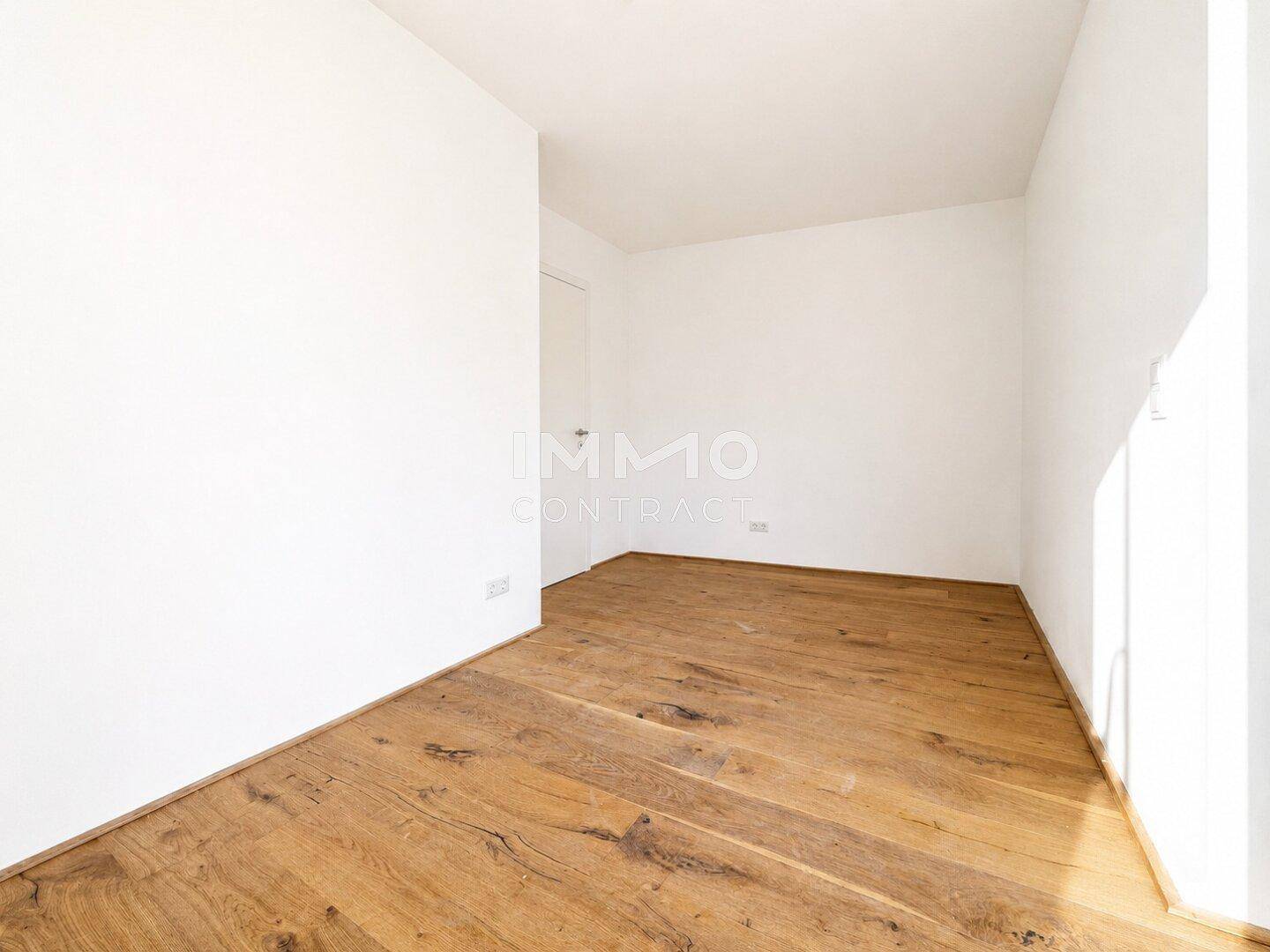 Heller Flur mit Holzboden und weißen Wänden, der zu weiteren Räumen führt.