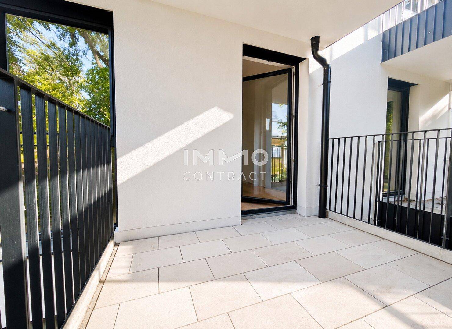 Heller Balkon mit Fliesenboden und schwarzem Geländer, zugänglich von einem Innenraum.