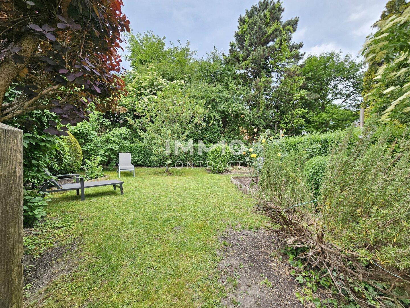Ruhiger Gartenbereich mit Rasenfläche, Sträuchern und einer kleinen Sitzecke zum Entspannen.