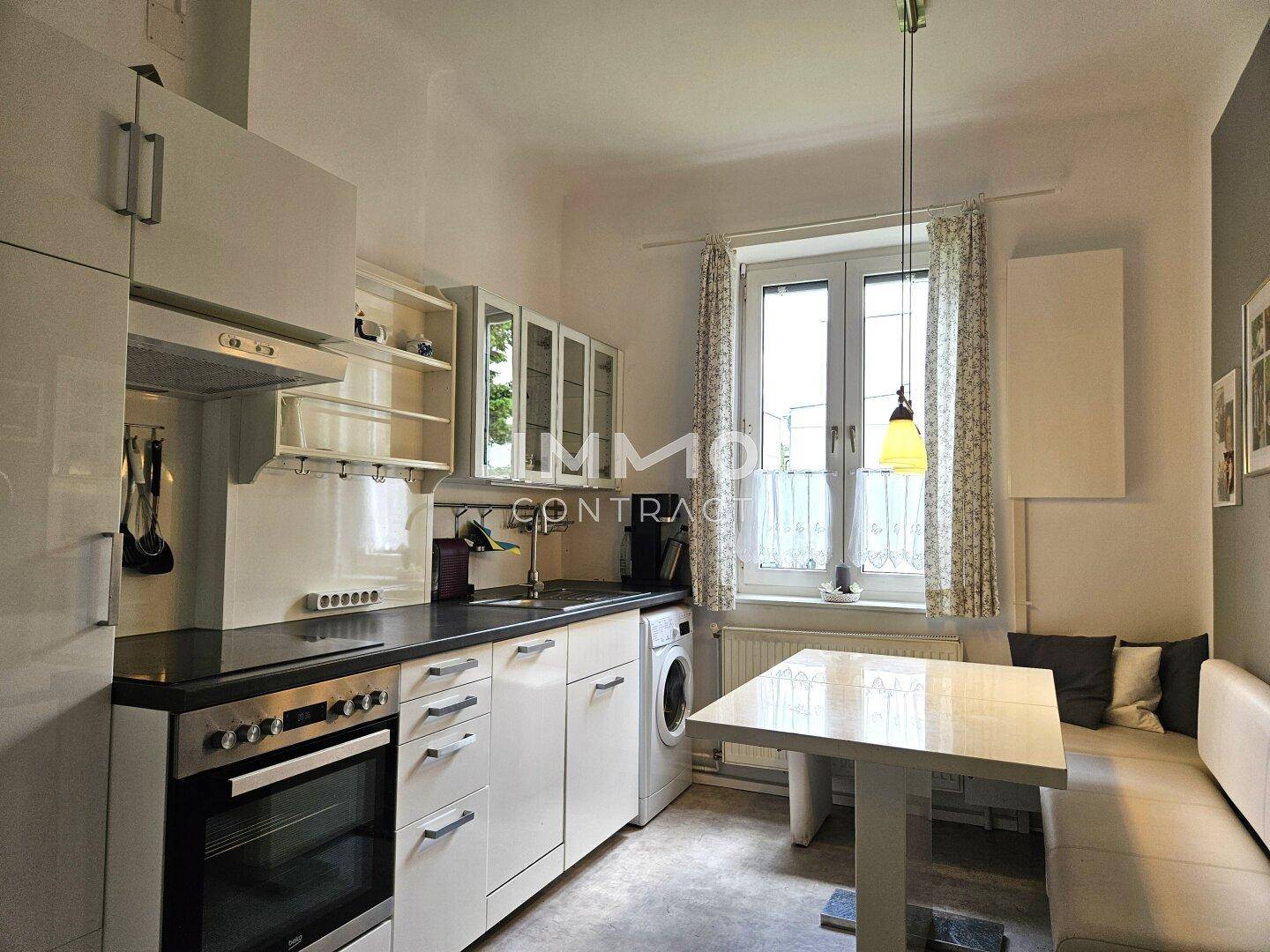 Helle Küche mit weißen Schränken, integriertem Backofen und einem gemütlichen Essbereich am Fenster.