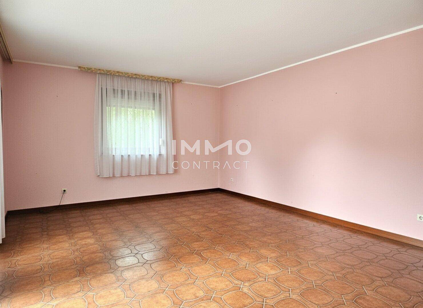 Leerer Raum mit rosa Wänden, gemusterten Fliesen und einem Fenster mit Vorhängen.