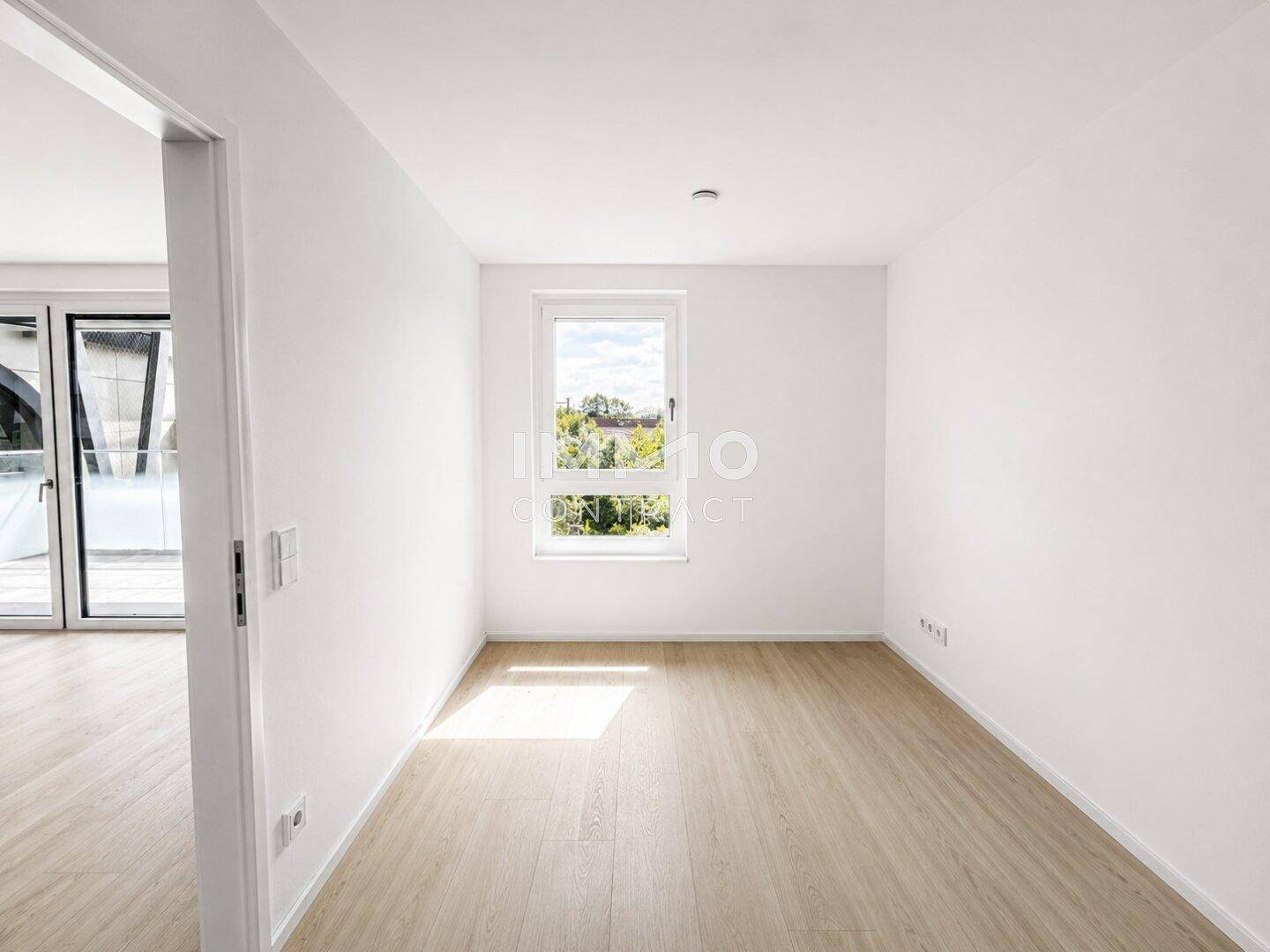 Helles Schlafzimmer mit Holzboden, weißen Wänden und einem Fenster mit Blick ins Grüne.