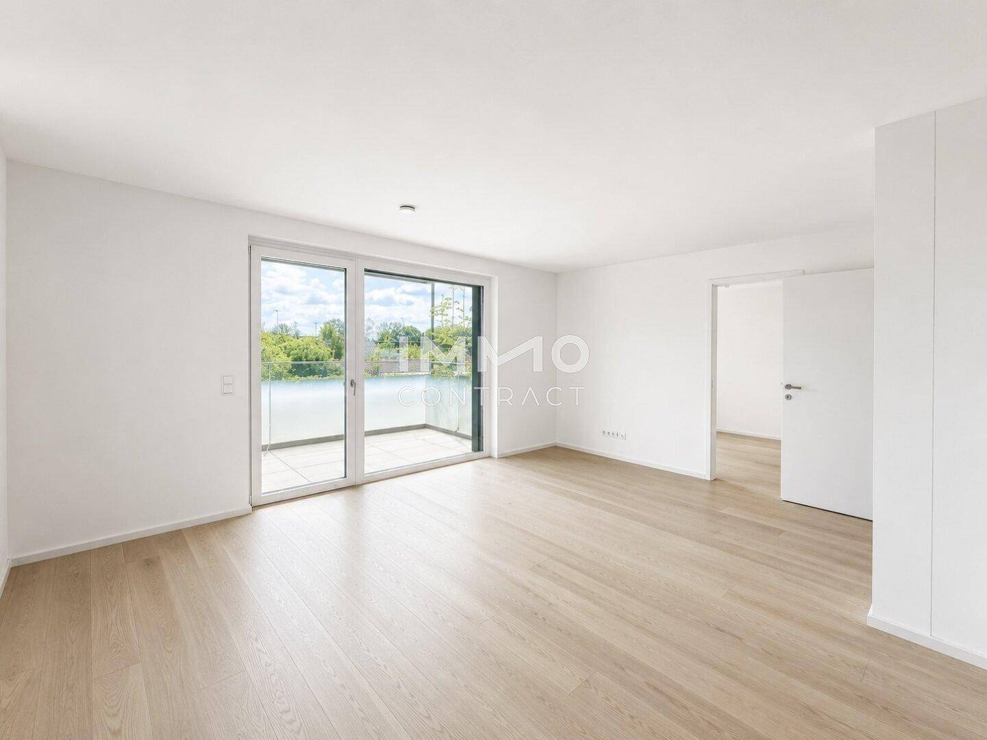 Heller, leerer Raum mit hellem Holzboden und großem Schiebefenster zum Balkon.
