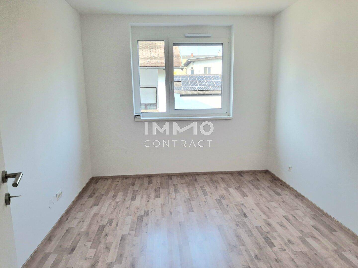 Freundliches, unmöbliertes Zimmer mit Laminatboden und einem großen Fenster für viel Tageslicht.
