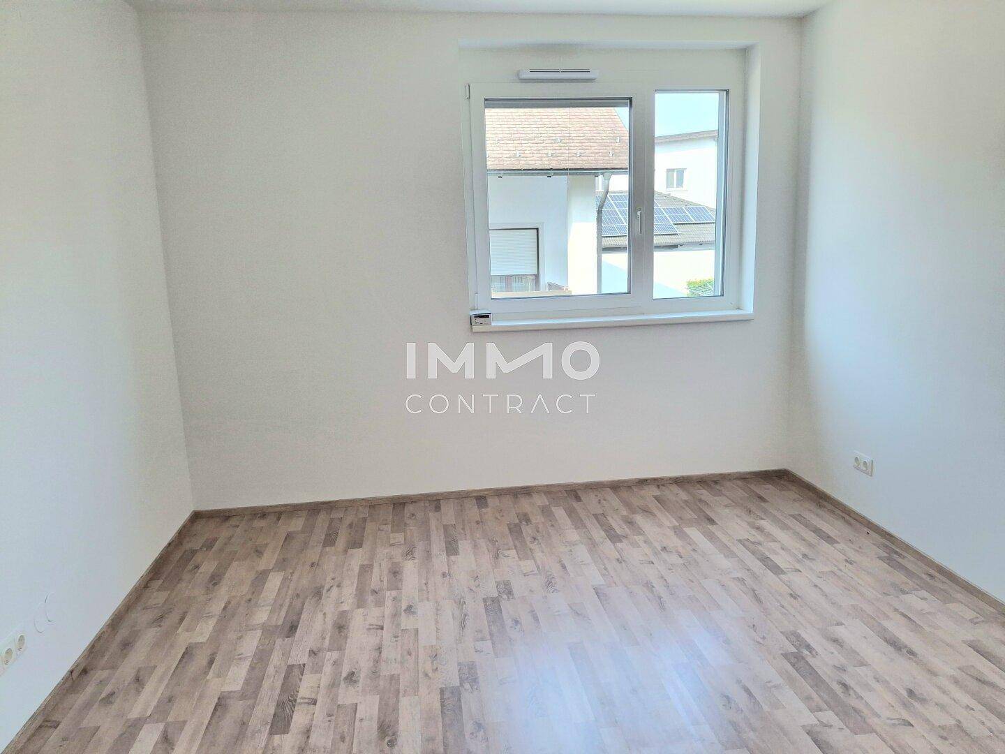 Helles, leeres Schlafzimmer mit Laminatboden und einem Fenster mit Blick nach draußen.
