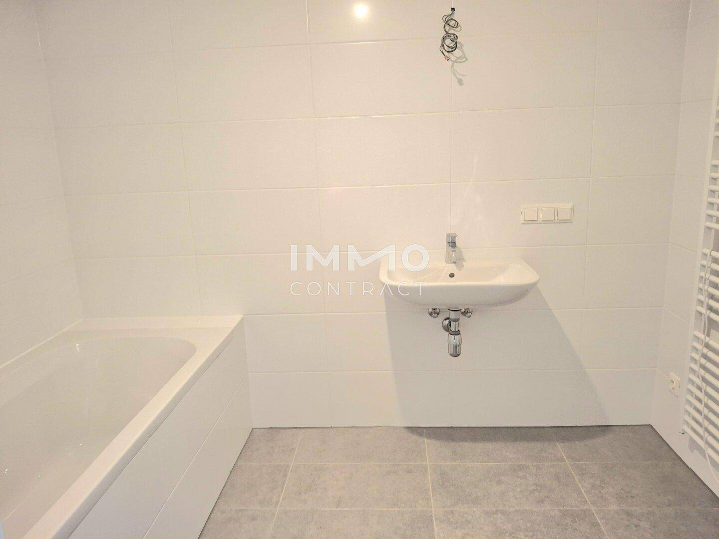 Modernes Badezimmer mit weißen Fliesen, Badewanne, Waschbecken und beheiztem Handtuchhalter.