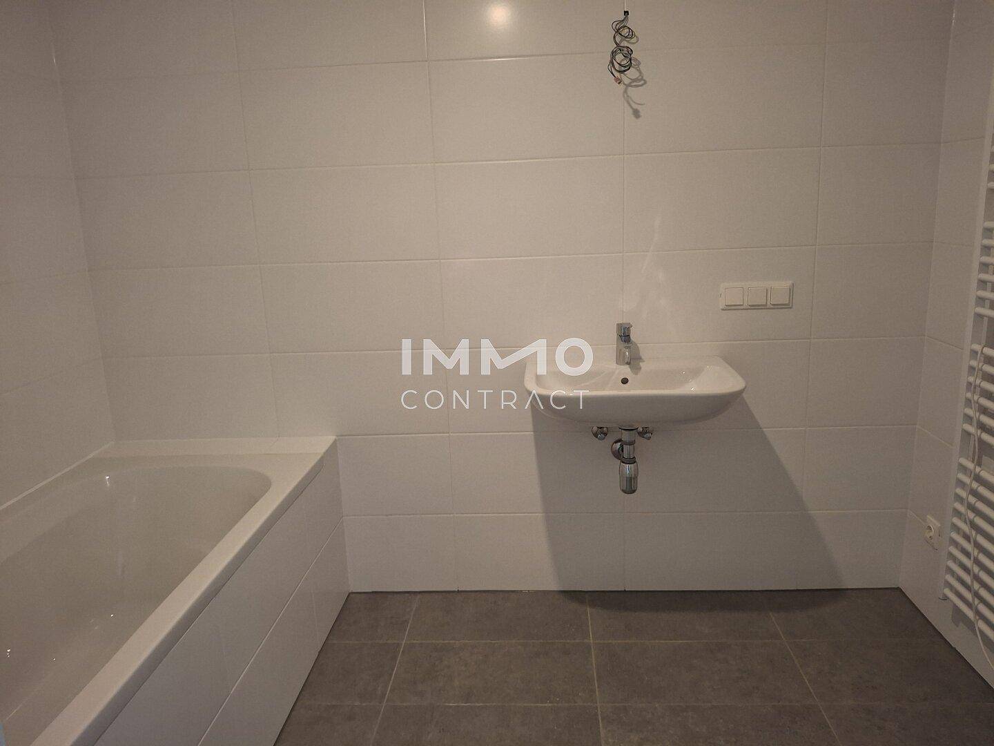 Sauberes Badezimmer mit weißen Wandfliesen, Badewanne, Waschbecken und Heizkörper.