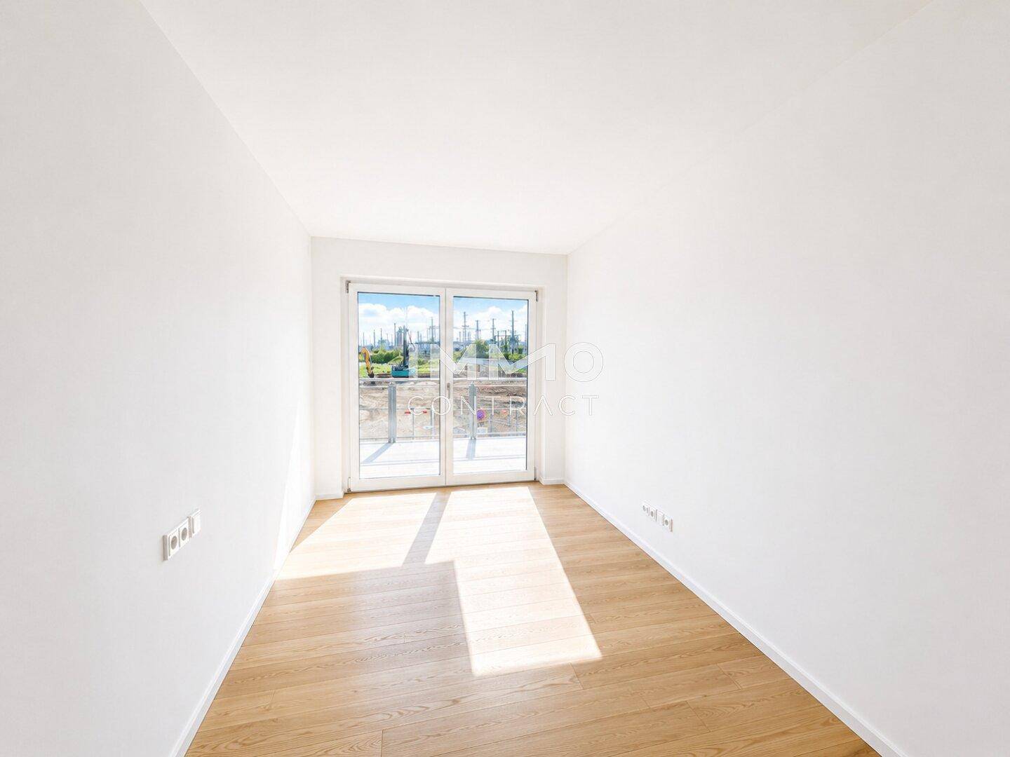 Lichtdurchfluteter Raum mit Holzboden und großen Fenstern mit Blick ins Freie.