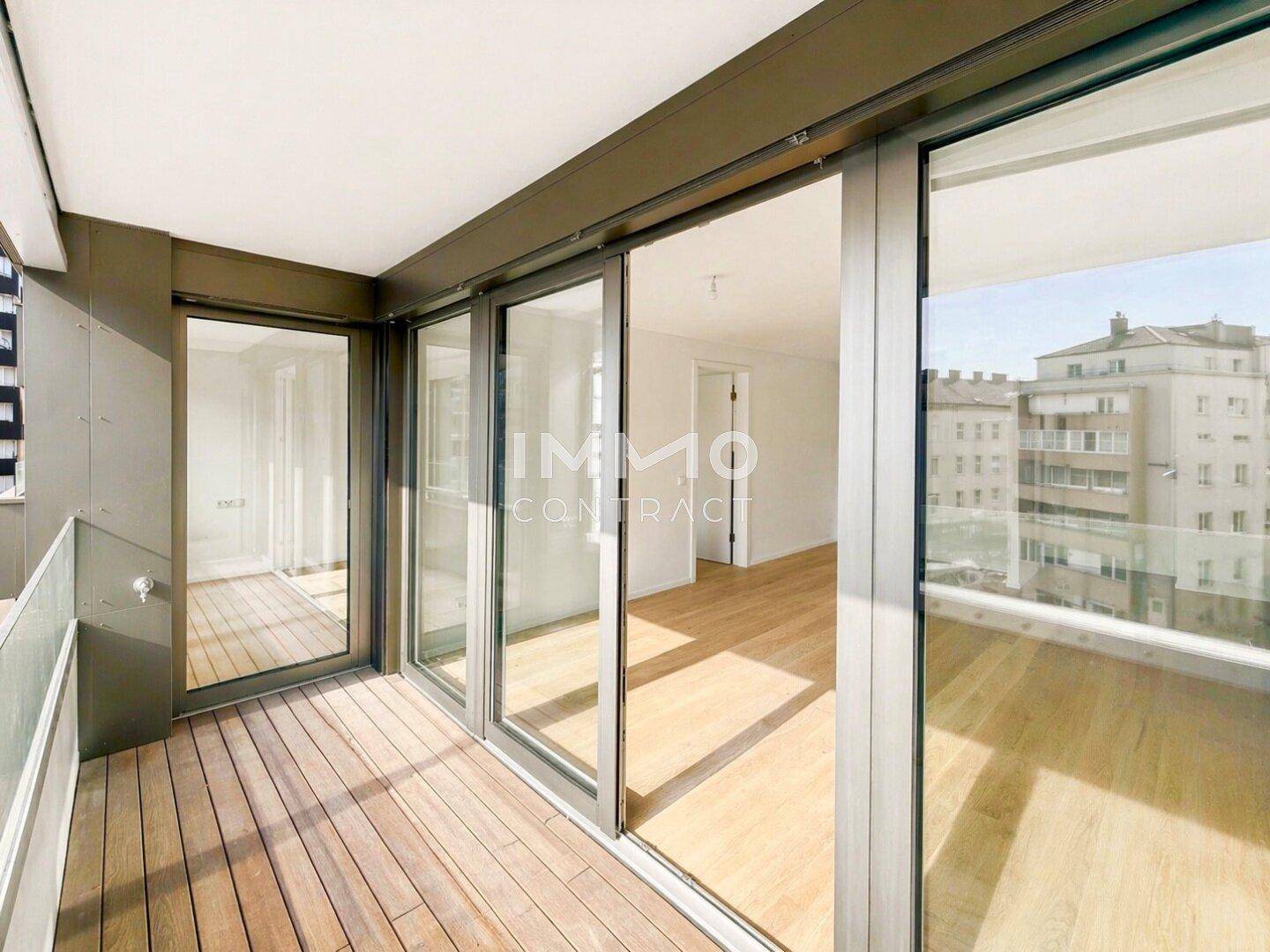 Geräumiger Balkon mit Holzboden und Glasgeländer, bietet einen weiten Blick auf die Stadt.