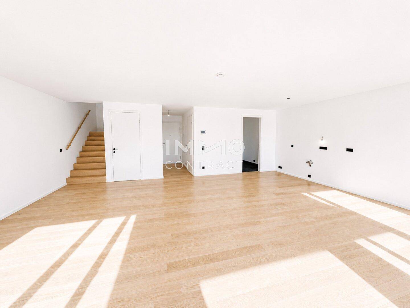 Geräumiger, heller Wohnbereich mit Holzboden und offener Verbindung zum Treppenhaus.