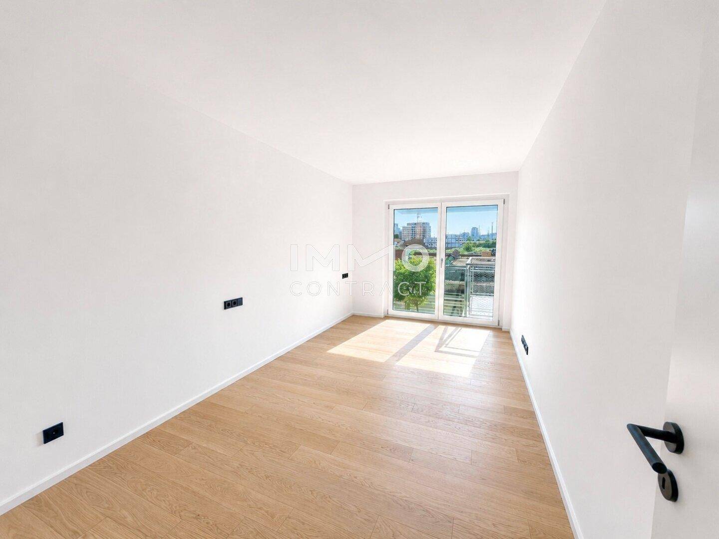 Helles Schlafzimmer mit Holzboden und großem Fenster, das viel Tageslicht hereinlässt.
