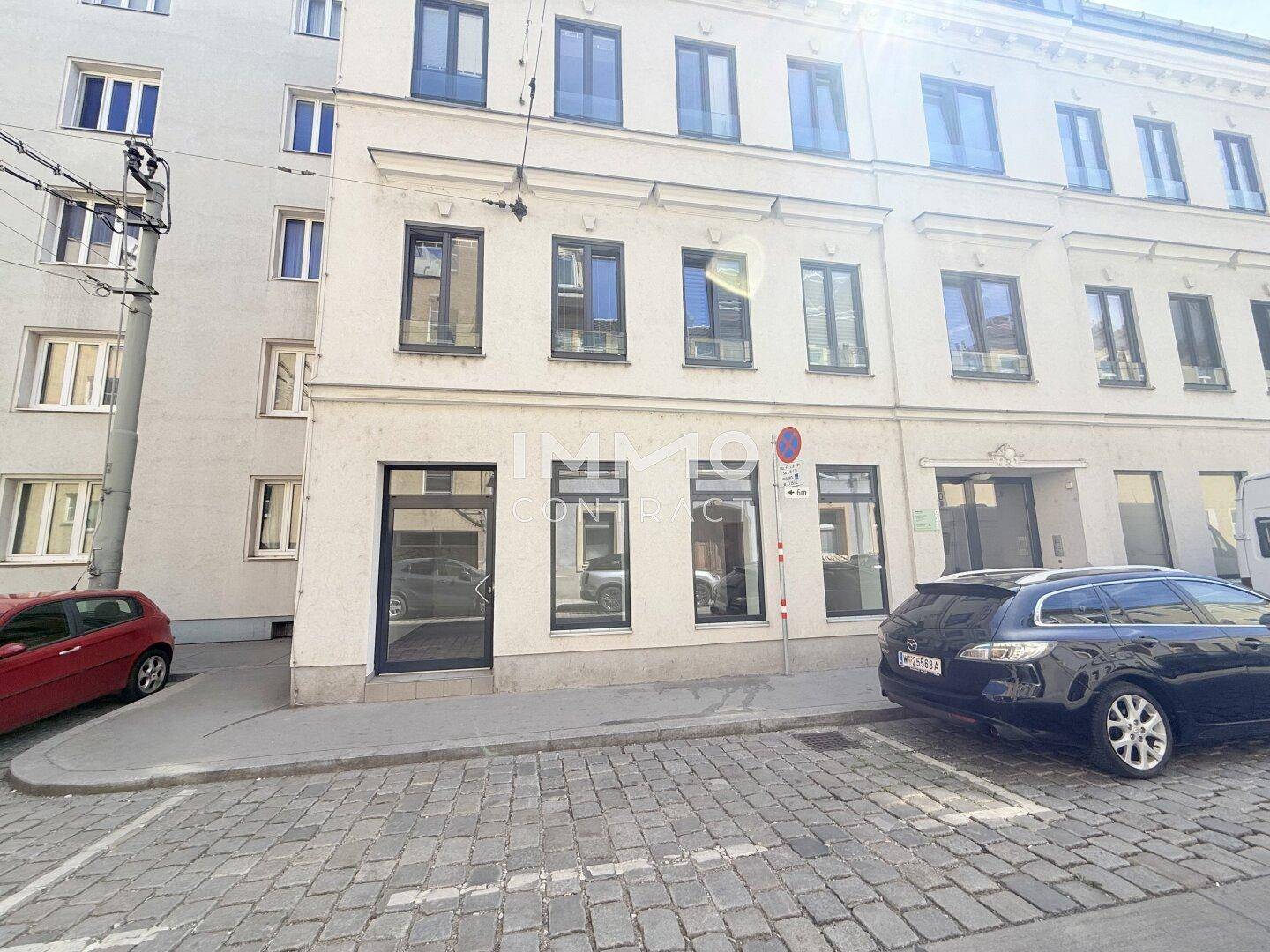 Gesamtansicht der Gebäudefassade mit Geschäftseingang und parkenden Autos auf der Straße.