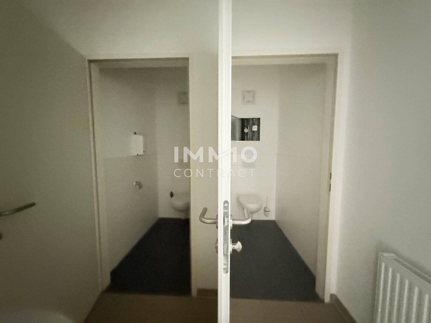 Zwei separate Toilettenräume mit weißen Wänden und dunklem Fliesenboden, funktional ausgestattet.