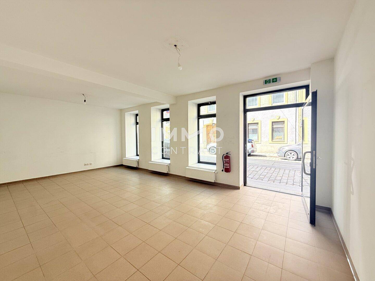 Heller und geräumiger Verkaufsraum mit großen Fenstern zur Straße und Fliesenboden.