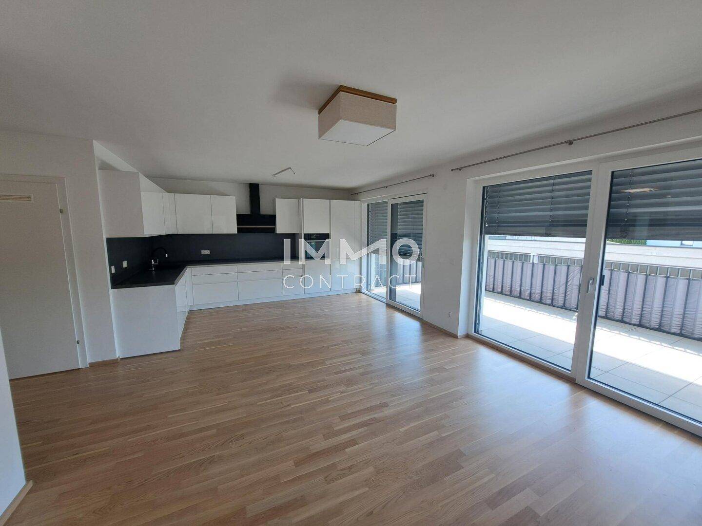 Offener Wohn-Ess-Küchenbereich mit Holzfußboden und großen Schiebetüren zum Balkon.